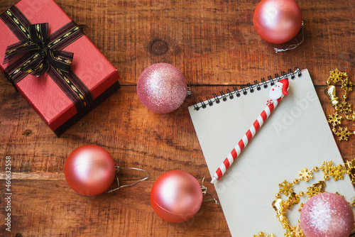 Christmas background. Pink Christmas balls, notebook, gift and golden garland on a wooden background.