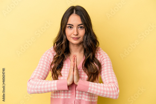 Young caucasian woman isolated on yellow background praying, showing devotion, religious person looking for divine inspiration. © Asier