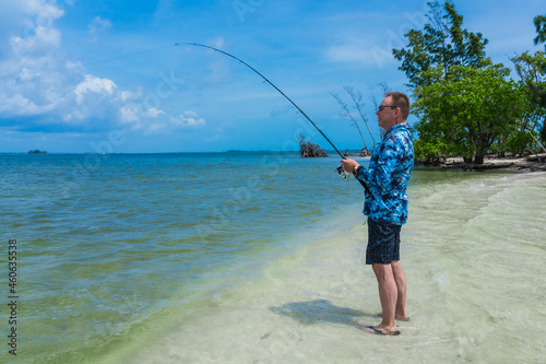 An elderly man in his 60s holds a fishing rod while fishing on a sandy island in the saltwater of the ocean on Indian River Island. Vero Beach, Florida