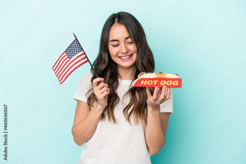 Young caucasian woman holding a hot dog isolated on blue background Young caucasian woman holding a hot dog isolated on blue background