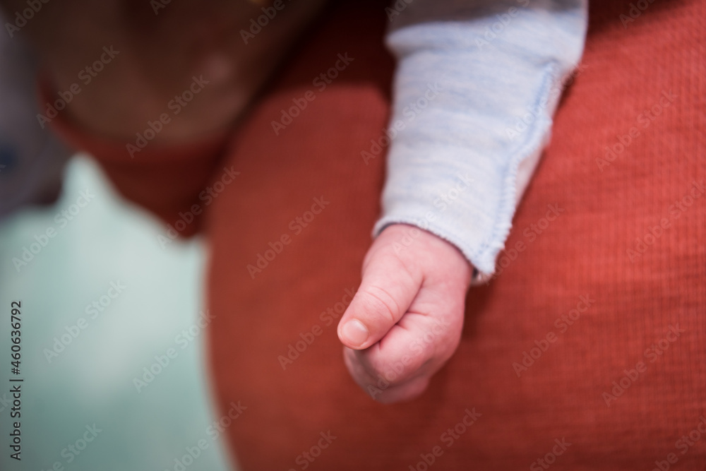 Close up. Little baby fist. Details. Dad's terracotta sweater in the background.