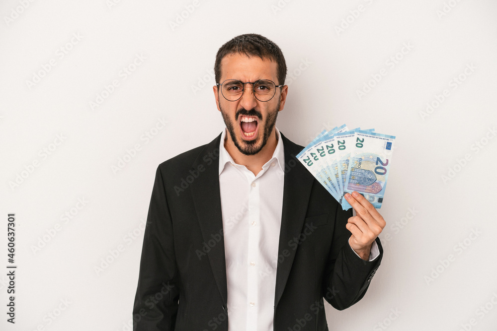 Young caucasian business man holding banknotes isolated on white background screaming very angry and aggressive. Young caucasian business man holding banknotes isolated on white background screaming very angry and aggressive.
