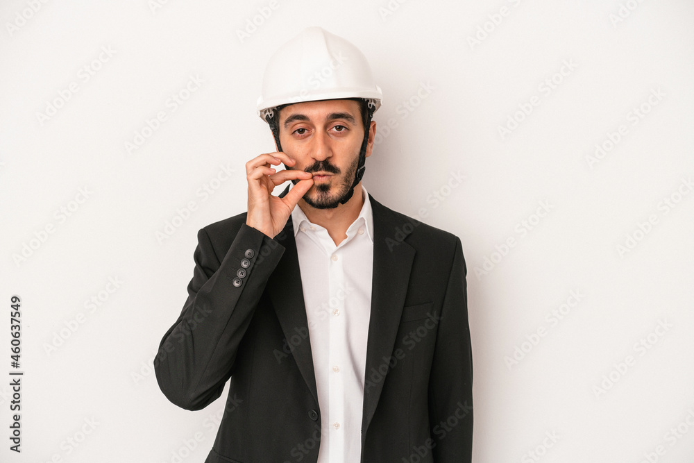 Young architect man wearing a construction helmet isolated on white background with fingers on lips keeping a secret.