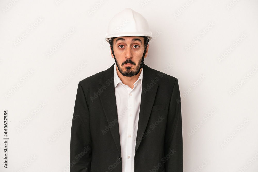 Young architect man wearing a construction helmet isolated on white background shrugs shoulders and open eyes confused. Young architect man wearing a construction helmet isolated on white background shrugs shoulders and open eyes confused.