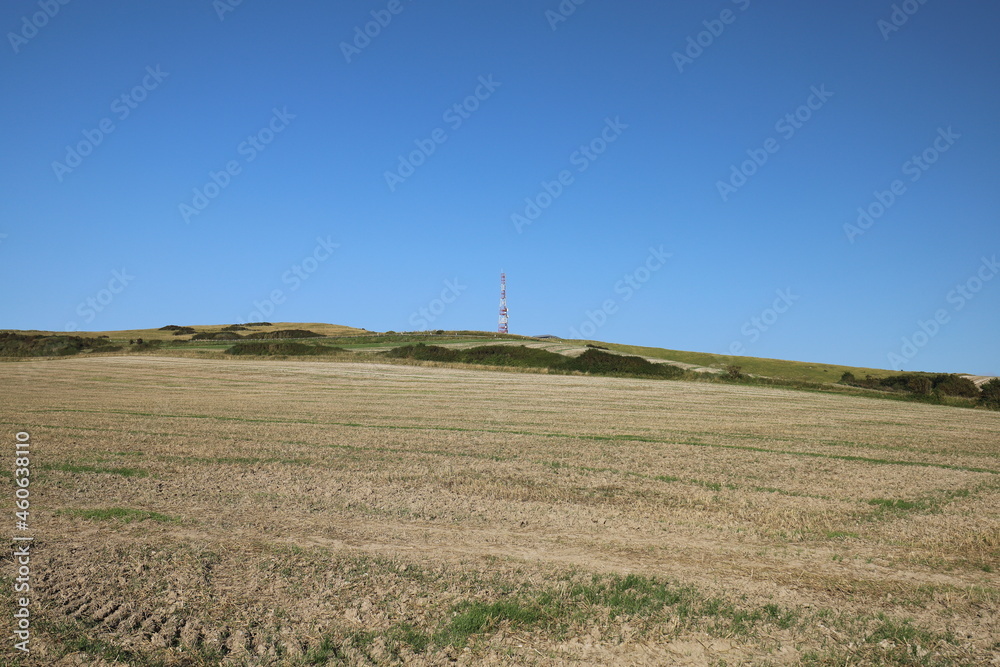 A transmission tower on a high hill in a green hilly landscape. Photo was taken on a sunny day with a blue sky. A transmission tower on a high hill in a green hilly landscape. Photo was taken on a sunny day with a blue sky.