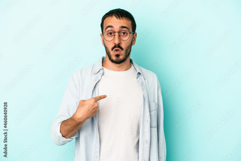 Young caucasian man isolated on blue background surprised pointing with finger, smiling broadly. Young caucasian man isolated on blue background surprised pointing with finger, smiling broadly.