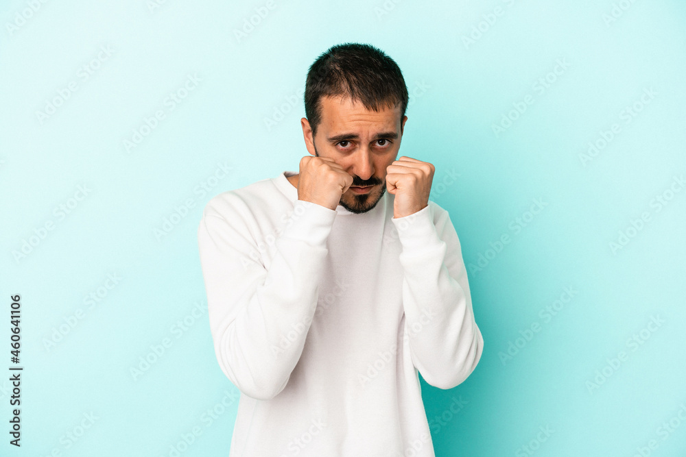 Young caucasian man isolated on blue background throwing a punch, anger, fighting due to an argument, boxing. Young caucasian man isolated on blue background throwing a punch, anger, fighting due to an argument, boxing.