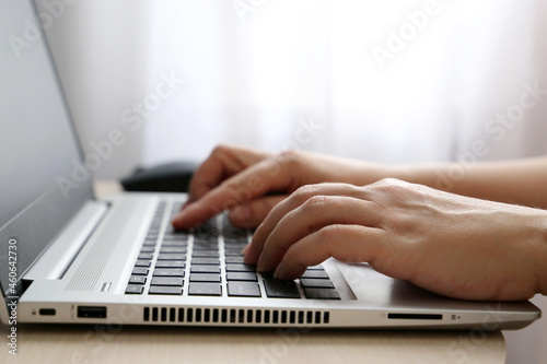 Female hands on laptop keyboard on a desk in sunlight. Woman types on the laptop keyboard sitting near the window, remote work