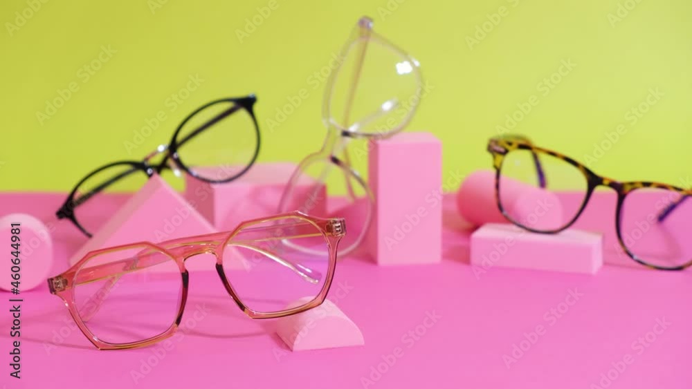 multiple eyeglasses on a pink ang yellow background, geometric stands, trendy eyeglass frames rolling geometric podiums multiple eyeglasses on a pink ang yellow background, geometric stands, trendy eyeglass frames rolling geometric podiums