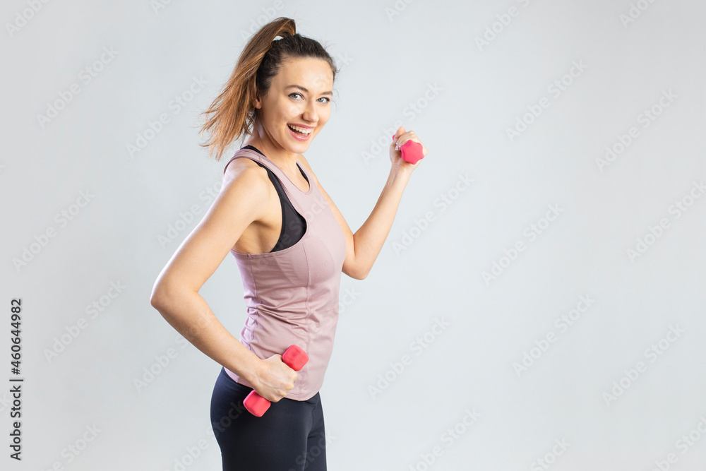 Young sporty woman exercising with dumbbells over gray background . Young sporty woman exercising with dumbbells over gray background .