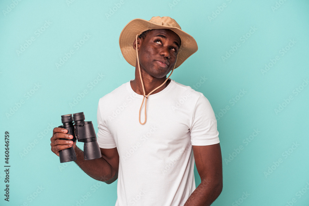 Young African American man holding binoculars isolated on blue background dreaming of achieving goals and purposes Young African American man holding binoculars isolated on blue background dreaming of achieving goals and purposes