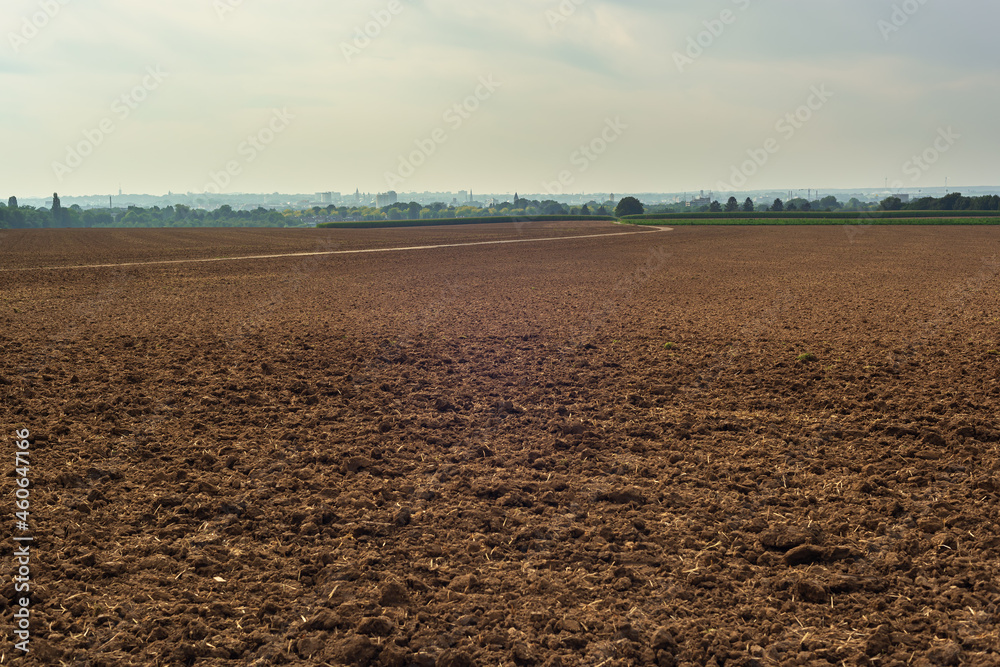 Bare arable field with a skyline of trees and a city under a cloudy sky. Bare arable field with a skyline of trees and a city under a cloudy sky.