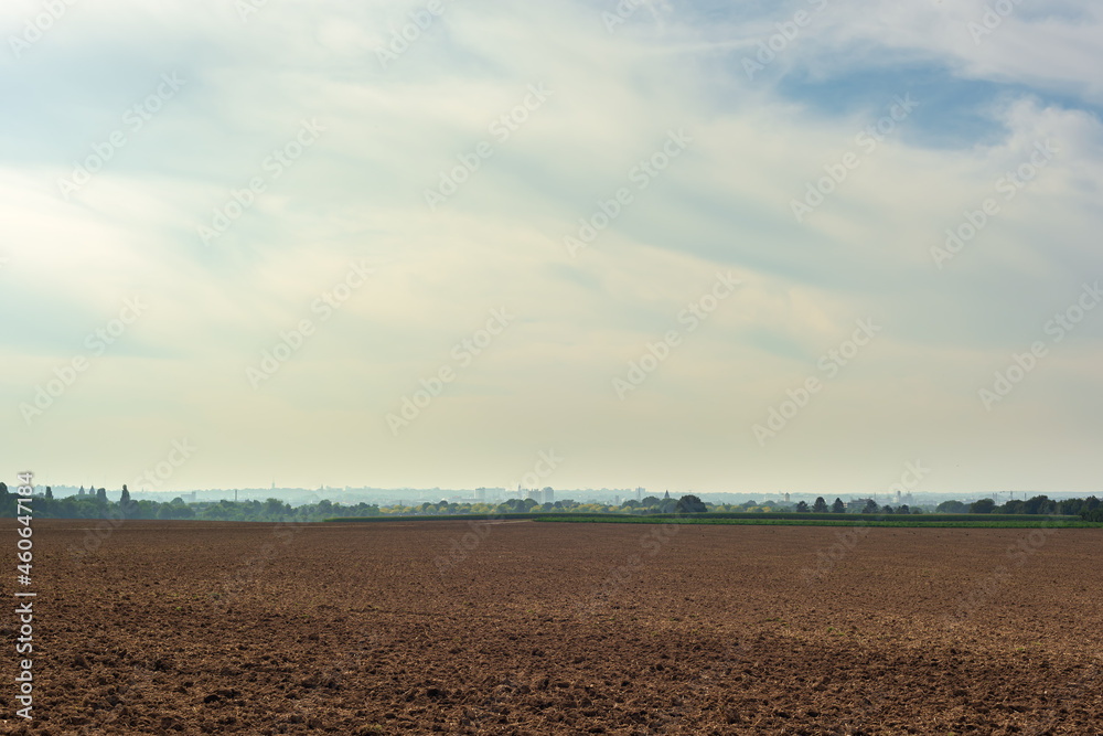 Bare arable field with a skyline of trees and a city under a cloudy sky. Bare arable field with a skyline of trees and a city under a cloudy sky.