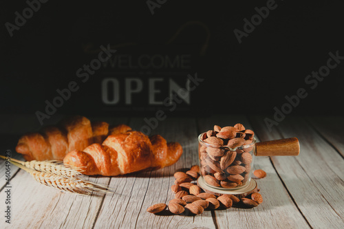 Freshly organic almonds with baked croissants on brown wooden table. Object on wooden table. Dark tone and open sign