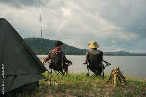 Friendship fisherman or Angler sitting a chair together and camping to fishing at the lake. Camping tent on the shore of the lake. Survival concept.