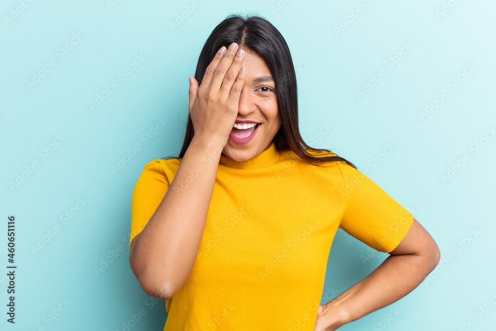 Young Venezuelan woman isolated on blue background having fun covering half of face with palm. Young Venezuelan woman isolated on blue background having fun covering half of face with palm.