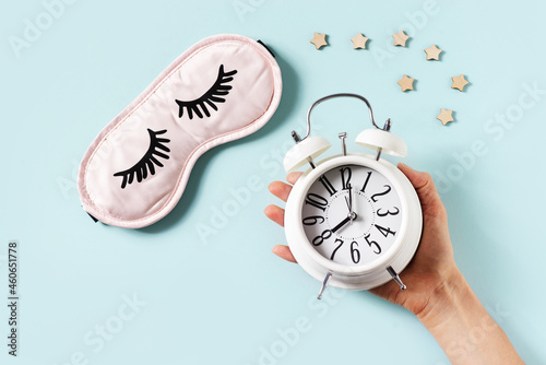 Sleep concept with mask, woman hand and alarm on blue background photo