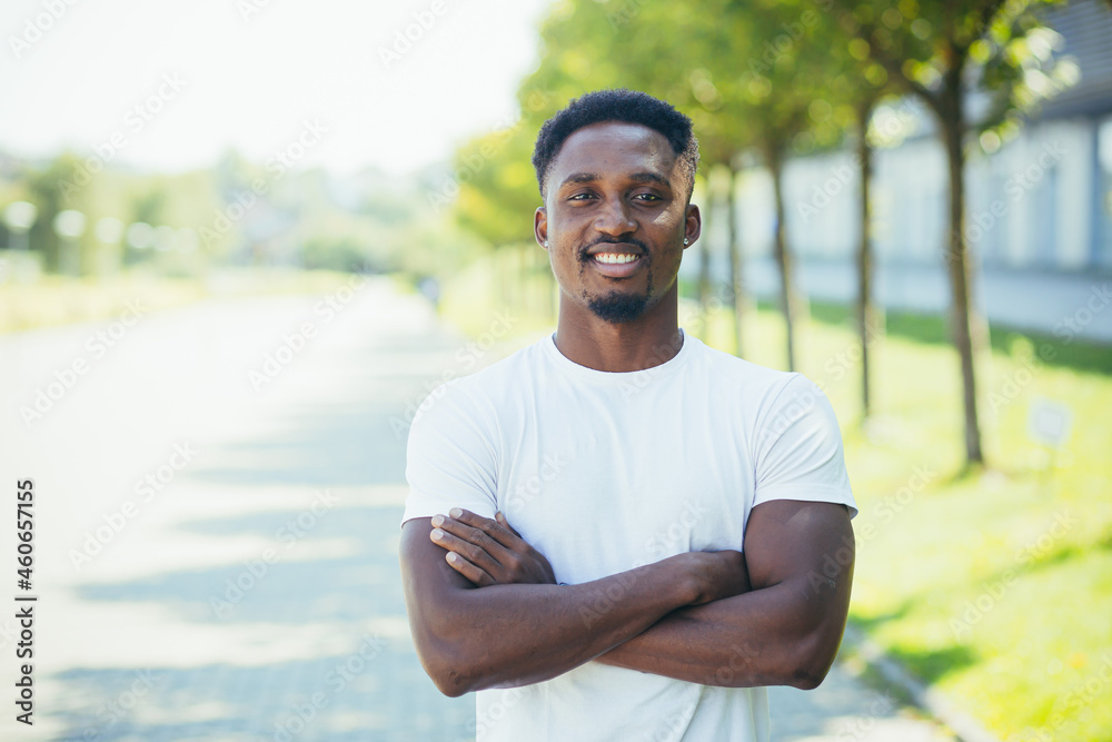 Fototapeta premium Young african american male athlete, on a morning jog, looks at the camera with his arms crossed, motivated and smiling