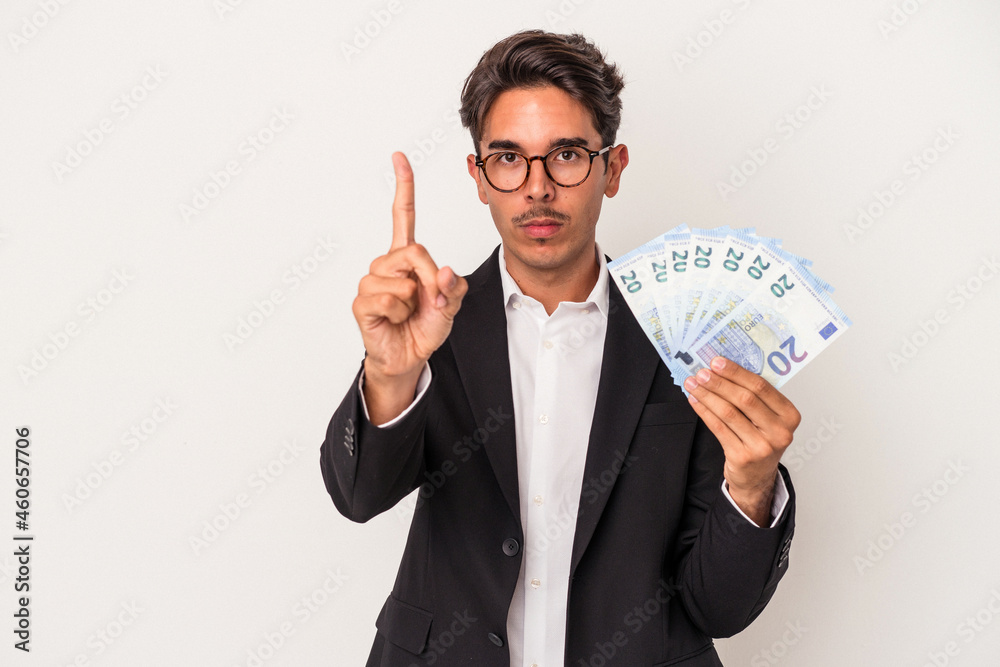 Young mixed race business man holding bills isolated on white background showing number one with finger. Young mixed race business man holding bills isolated on white background showing number one with finger.
