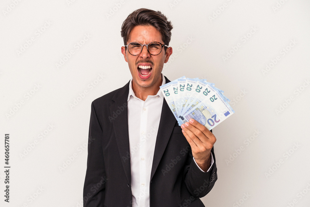 Young mixed race business man holding bills isolated on white background screaming very angry and aggressive. Young mixed race business man holding bills isolated on white background screaming very angry and aggressive.