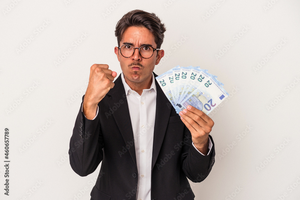 Young mixed race business man holding bills isolated on white background showing fist to camera, aggressive facial expression. Young mixed race business man holding bills isolated on white background showing fist to camera, aggressive facial expression.