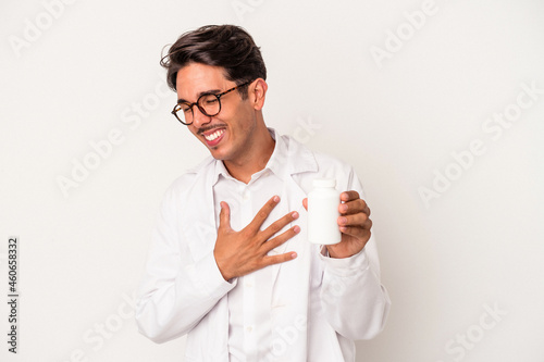 Young pharmacist mixed race man holding pills isolated on white background laughing and having fun.