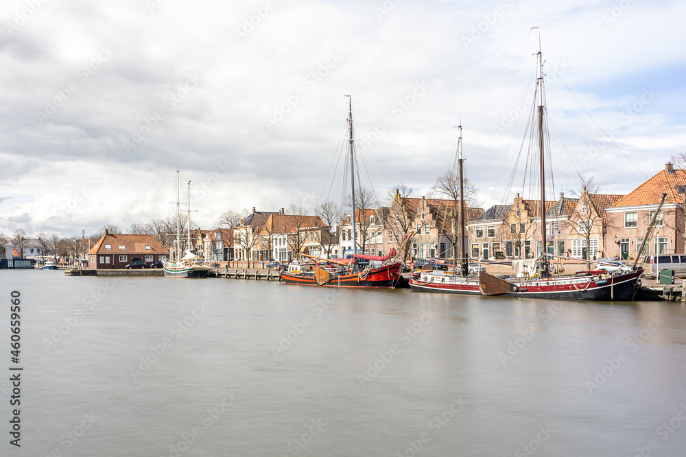 Oosterhaven quay in the city harbor, anchored boats, houses and buildings in the background, cloudy day with stormy clouds in Medemblik, Noord-Holland, Netherlands. Long exposure photography