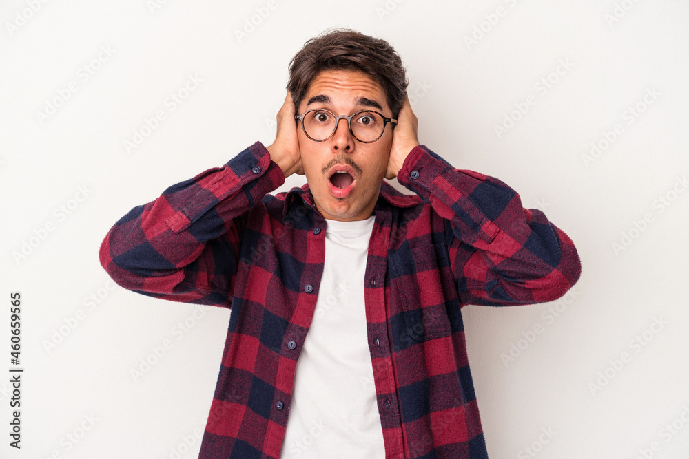Young mixed race man isolated on white background covering ears with hands trying not to hear too loud sound. Young mixed race man isolated on white background covering ears with hands trying not to hear too loud sound.