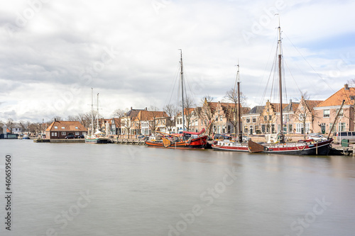 Oosterhaven quay in the city harbor, anchored boats, houses and buildings in the background, cloudy day with stormy clouds in Medemblik, Noord-Holland, Netherlands. Long exposure photography