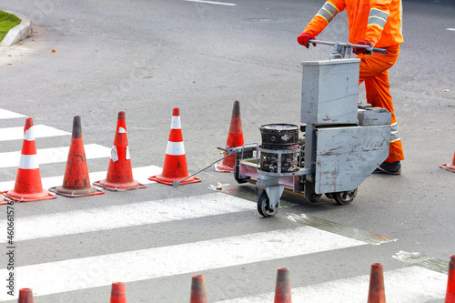 A road worker uses a power trolley to renew the markings of a pedestrian crossing.