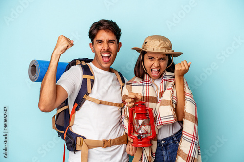 Young mixed race hiker couple isolated on blue background raising fist after a victory, winner concept.