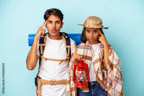 Young mixed race hiker couple isolated on blue background pointing temple with finger, thinking, focused on a task.