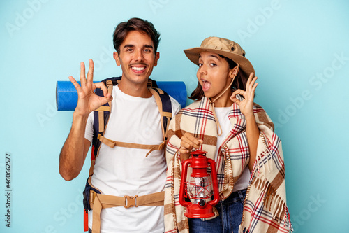 Young mixed race hiker couple isolated on blue background cheerful and confident showing ok gesture.