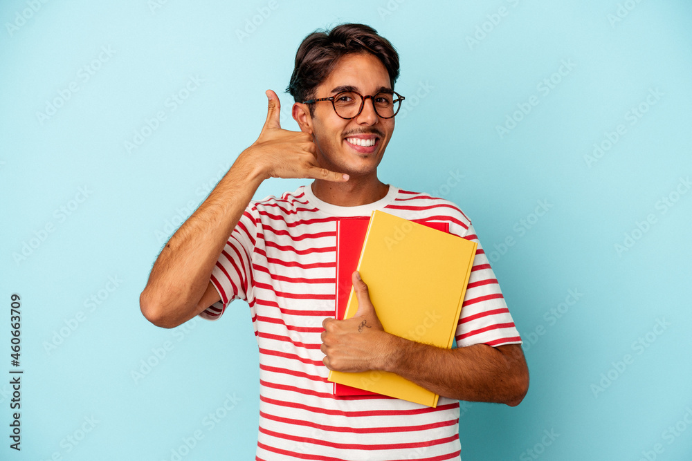 Young mixed race student man holding books isolated on blue background showing a mobile phone call gesture with fingers. Young mixed race student man holding books isolated on blue background showing a mobile phone call gesture with fingers.