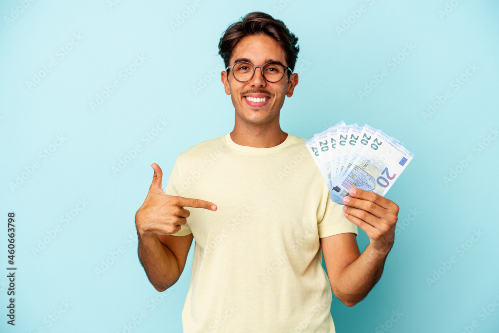 Young mixed race man holding bills isolated on blue background person pointing by hand to a shirt copy space, proud and confident Young mixed race man holding bills isolated on blue background person pointing by hand to a shirt copy space, proud and confident