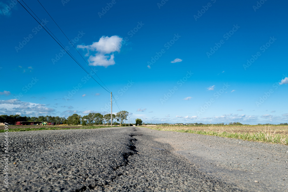 Ground level, shallow focus of severe tarmac subsidence seen in a rural road. Heavy farm machinery has accelerated the road surface damage.