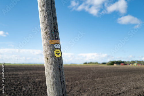  Leaning wooden telegraph pole in a rural location, near a distant farm. The pole advertises that it carries Fibre Optic Internet Broadband to a rural community photo
