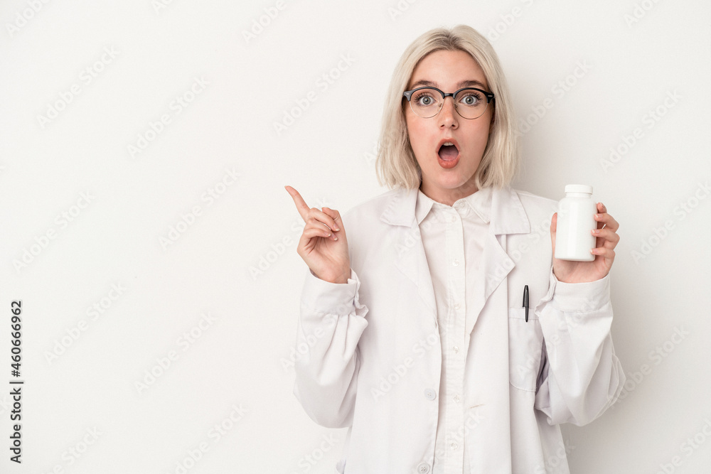 Young pharmacist woman holding pills isolated on white background pointing to the side Young pharmacist woman holding pills isolated on white background pointing to the side