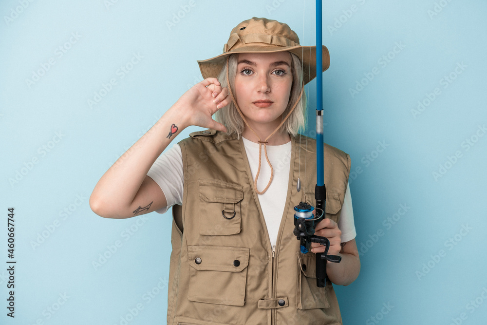 Young caucasian fisherwoman holding a rod isolated on blue background showing a dislike gesture, thumbs down. Disagreement concept. Young caucasian fisherwoman holding a rod isolated on blue background showing a dislike gesture, thumbs down. Disagreement concept.