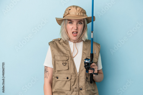 Young caucasian fisherwoman holding a rod isolated on blue background screaming very angry and aggressive.