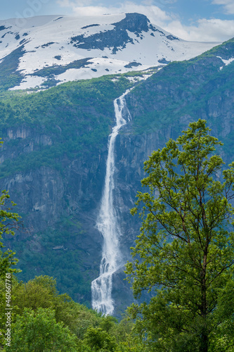 Spring view in Norway with tall snowdy mountain and waterfall together with green trees.