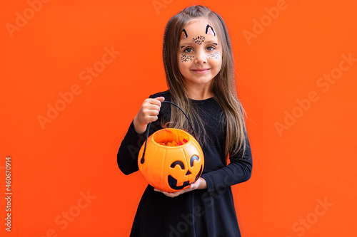 Funny child girl in costume for Halloween with pumpkin Jack isolated on orange background.