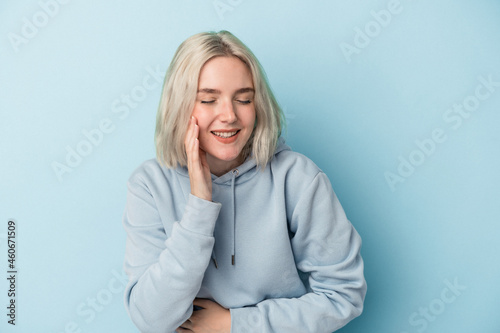 Young caucasian woman isolated on blue background laughs happily and has fun keeping hands on stomach.