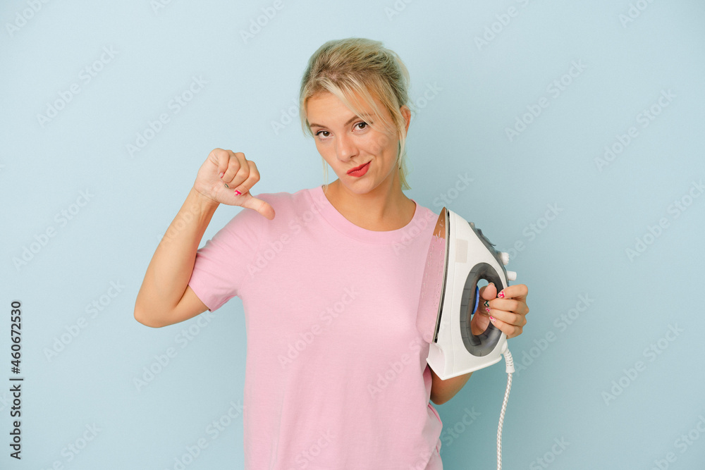Young Russian woman holding iron isolated on blue background feels proud and self confident, example to follow. Young Russian woman holding iron isolated on blue background feels proud and self confident, example to follow.
