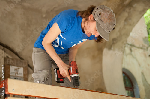 Skilled young female worker is using power screwdriver drilling during construction wooden bench gender equality, feminism, do it yourself concepts.