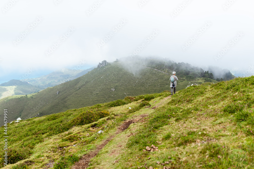 Senior hiker from behind with backpack walking up the mountain on a foggy day.