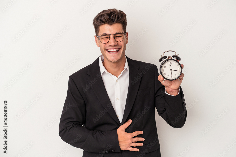 Young business caucasian man holding alarm clock isolated on white background laughing and having fun. Young business caucasian man holding alarm clock isolated on white background laughing and having fun.