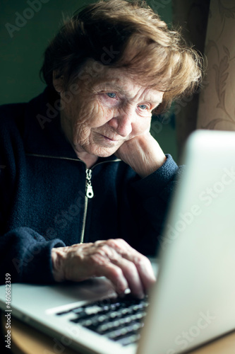 An old woman is typing on a laptop at her home.