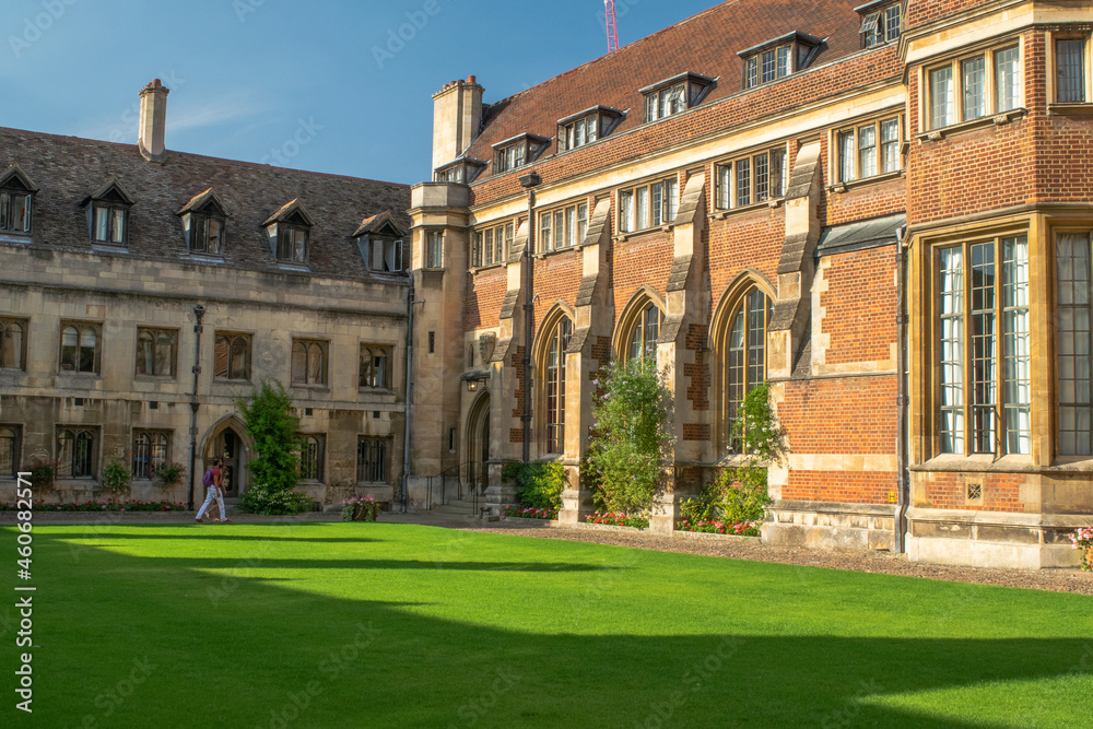 University Students walk along the lawn of historical bricked Christ's College Court with ornate entrance and medieval windows at Cambridge England