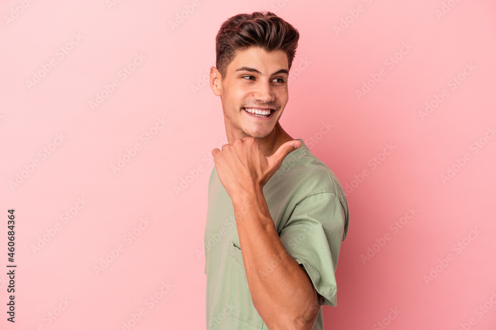 Obraz premium Young caucasian man isolated on pink background points with thumb finger away, laughing and carefree.